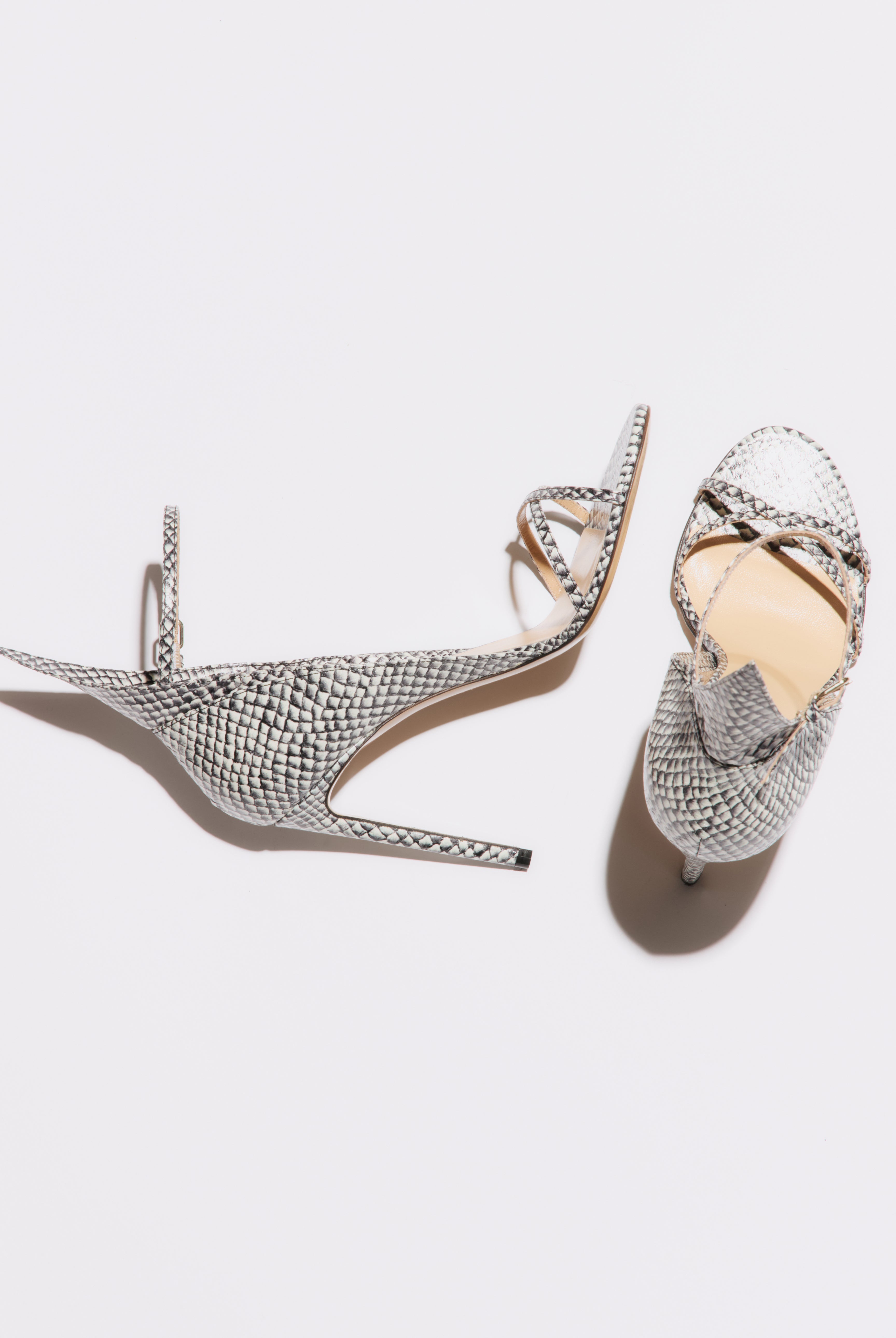 Pair of silver high-heeled shoes with intricate designs on a light gray background