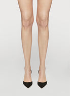 Legs wearing sheer beige stockings with black high heels on a light gray background