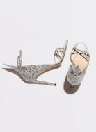 Pair of silver high-heeled shoes with intricate designs on a light gray background