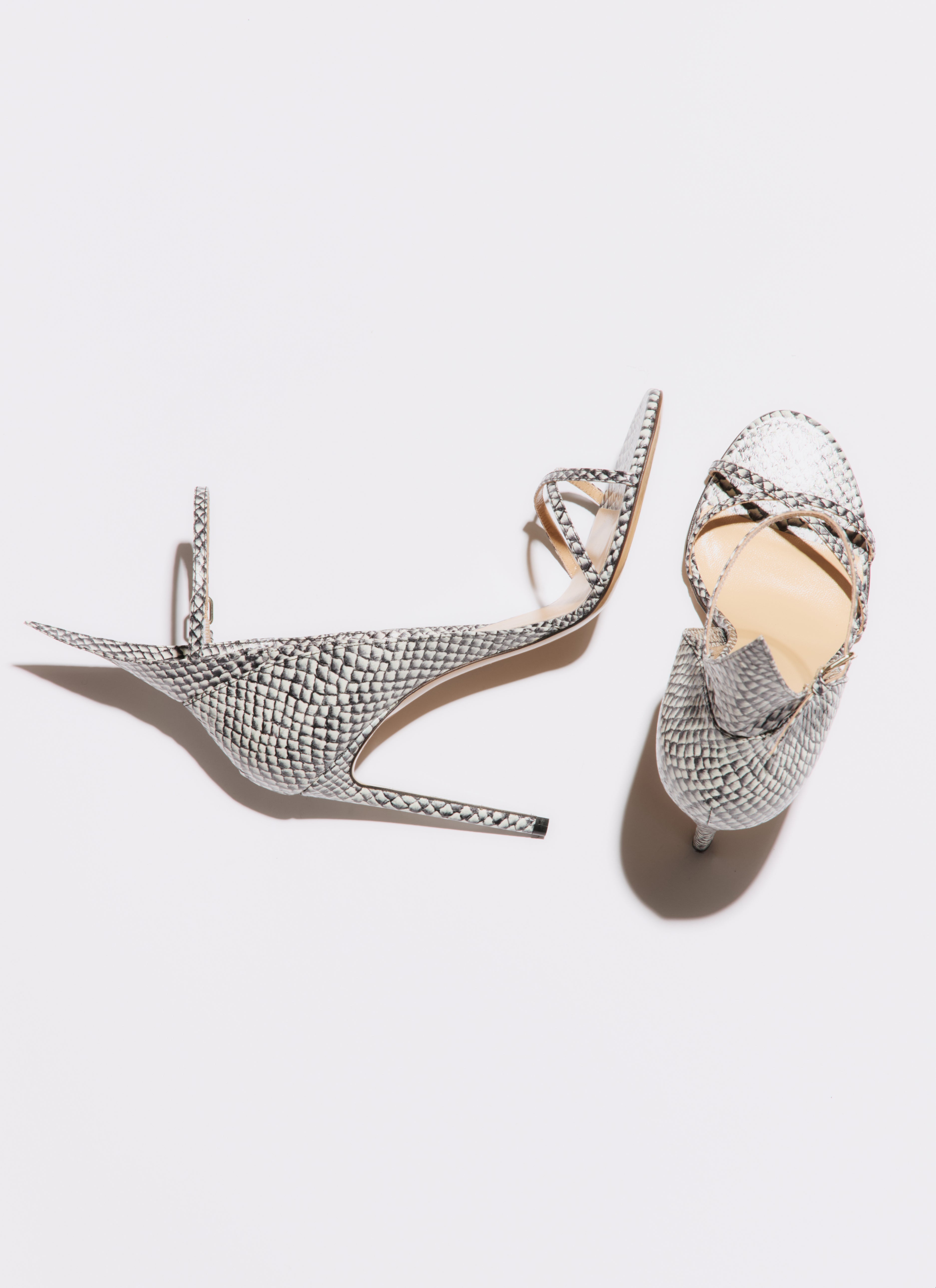 Pair of silver high-heeled shoes with intricate designs on a light gray background