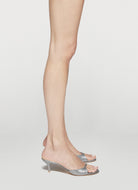 A pair of metallic silver mule sandals with kitten heels, shown on a model's feet against a light gray studio background.